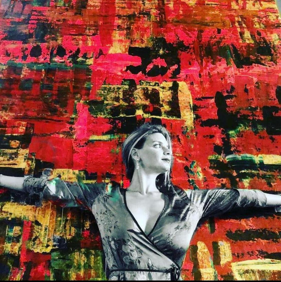 Polen Cerci with arms open before her red abstract paintings
